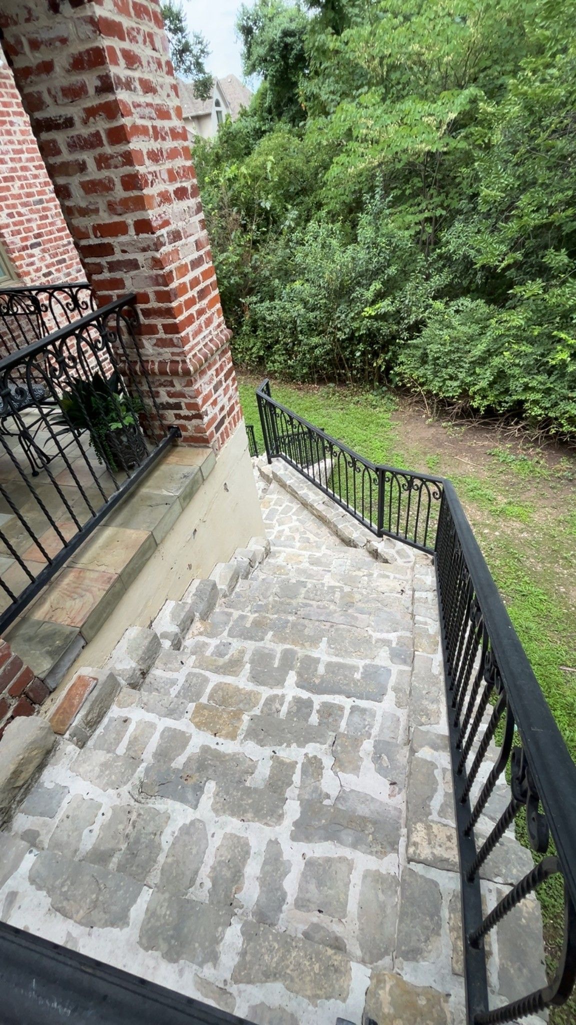 Brick stairway with black railings beside a brick building, leading down toward a green wooded area.