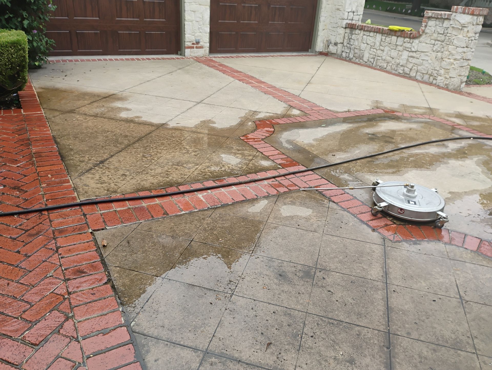 Wet driveway and brick walkway with a small robot vacuum near a garage door.