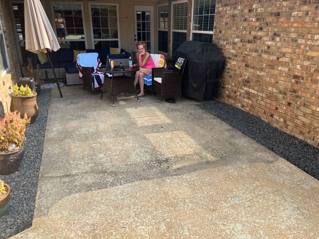 Back patio with table and chairs, a person sitting outside, potted plants, and a brick wall with a grill