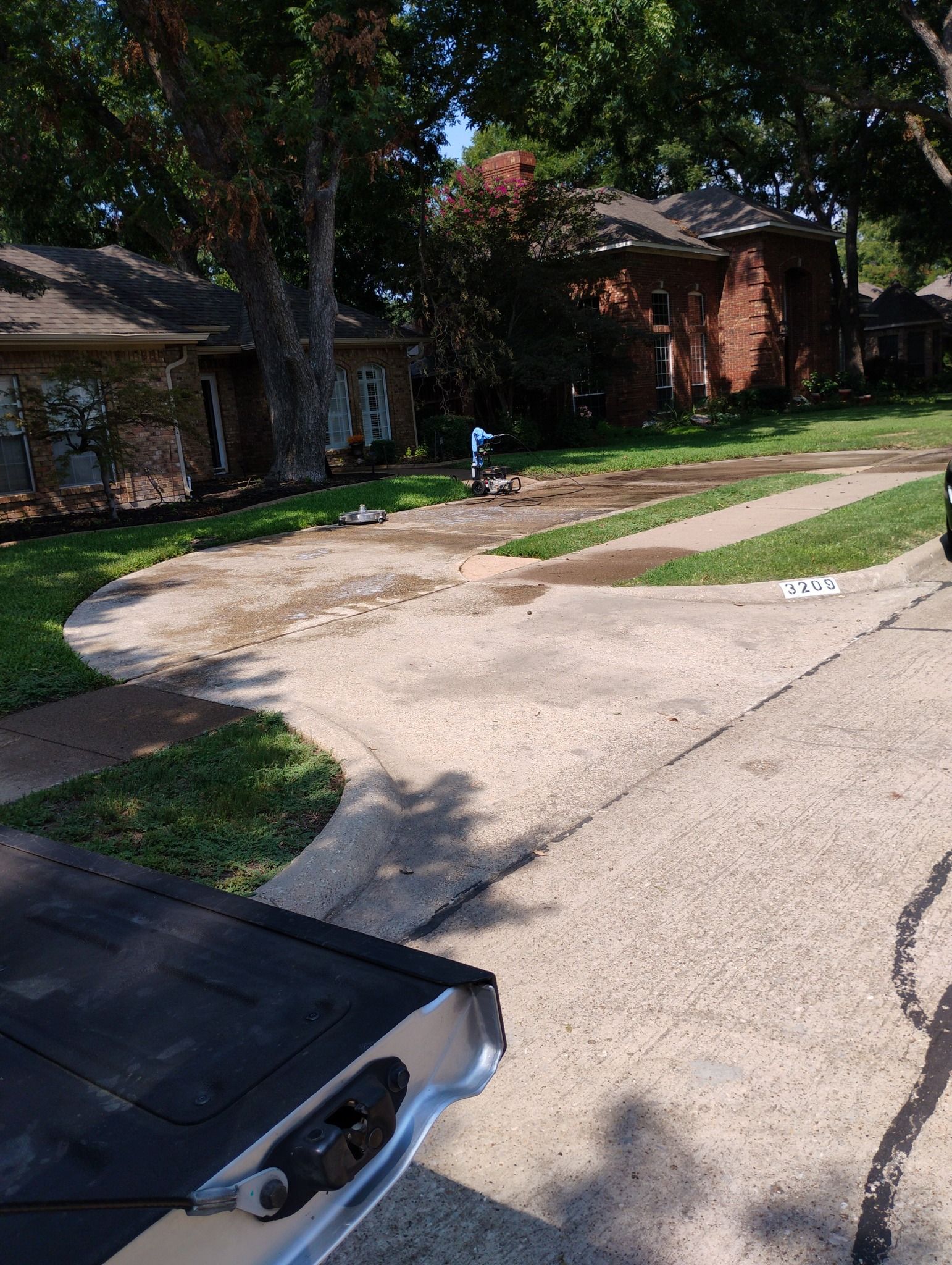 Driveway and front yard of a brick suburban house, with a concrete slab and a bench in the foreground.