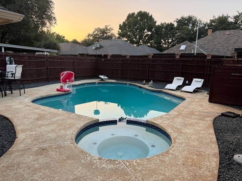 Backyard pool and hot tub at dusk with lounge chairs, red float, and a wooden privacy fence
