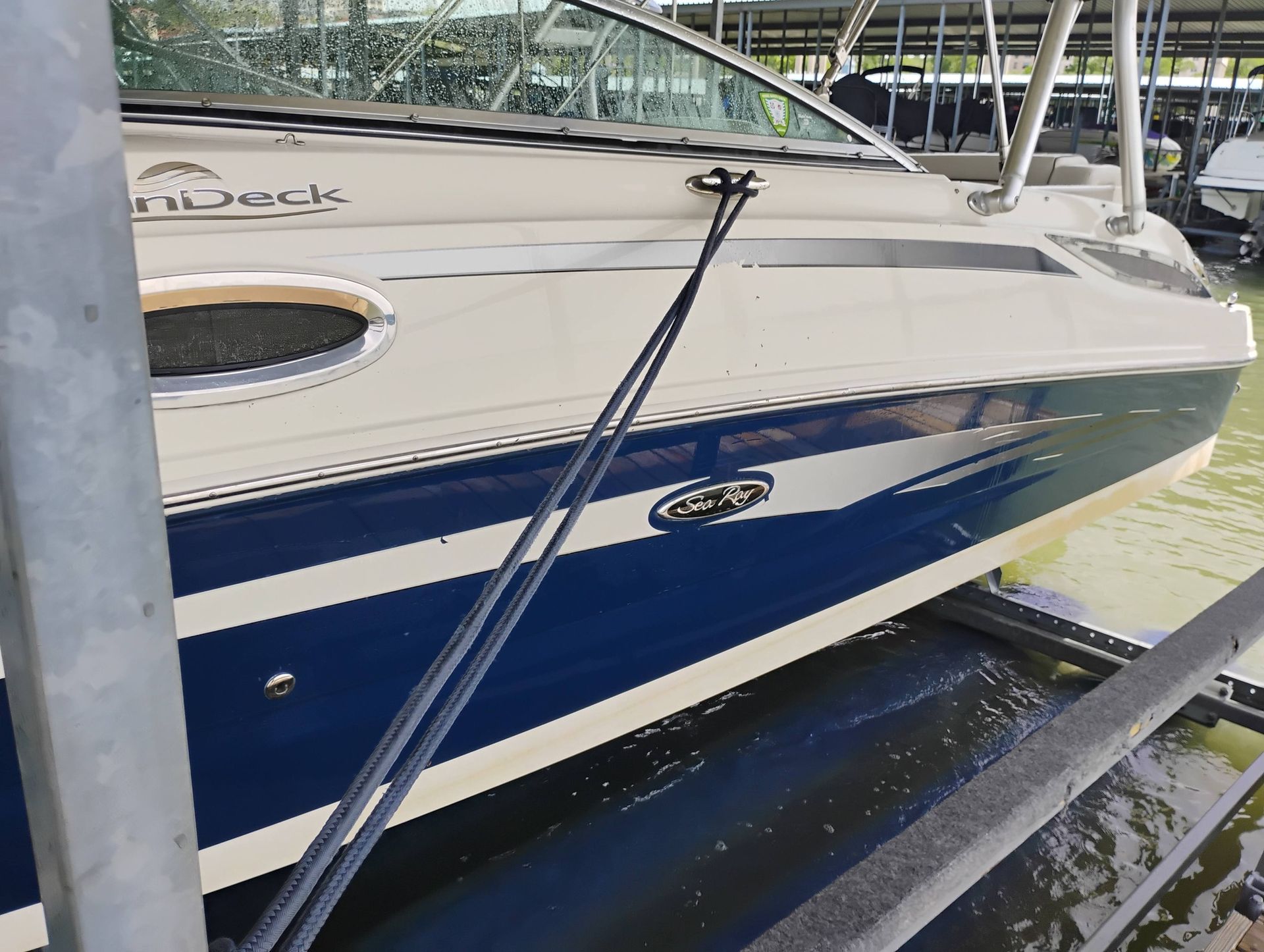 White and blue boat docked at a marina, secured with black mooring lines.