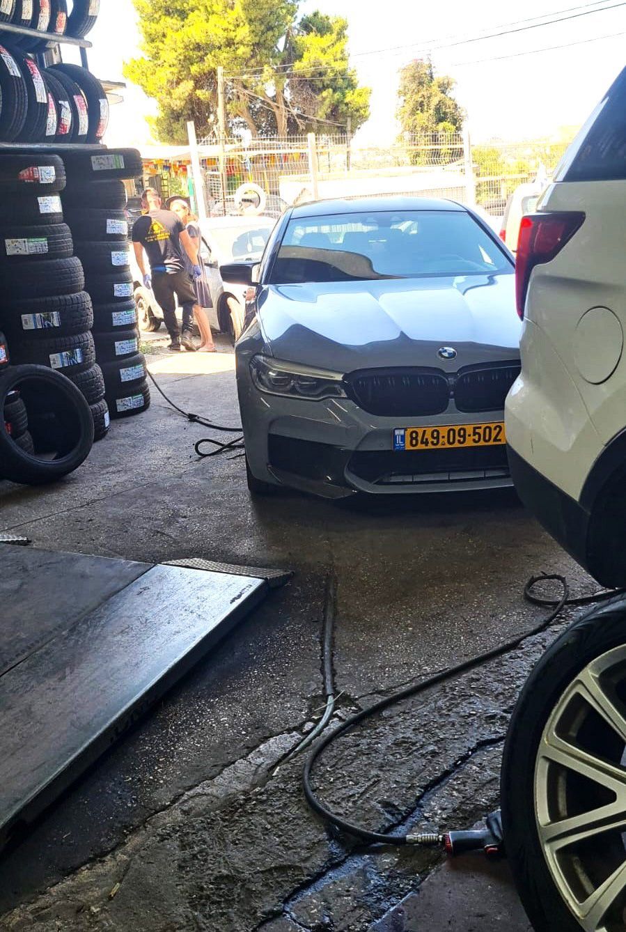 רכב ב.מ.וו אפור במהלך עבודות תיקון פנצ'ר בירושלים לצד רכב שטח בסדנה.