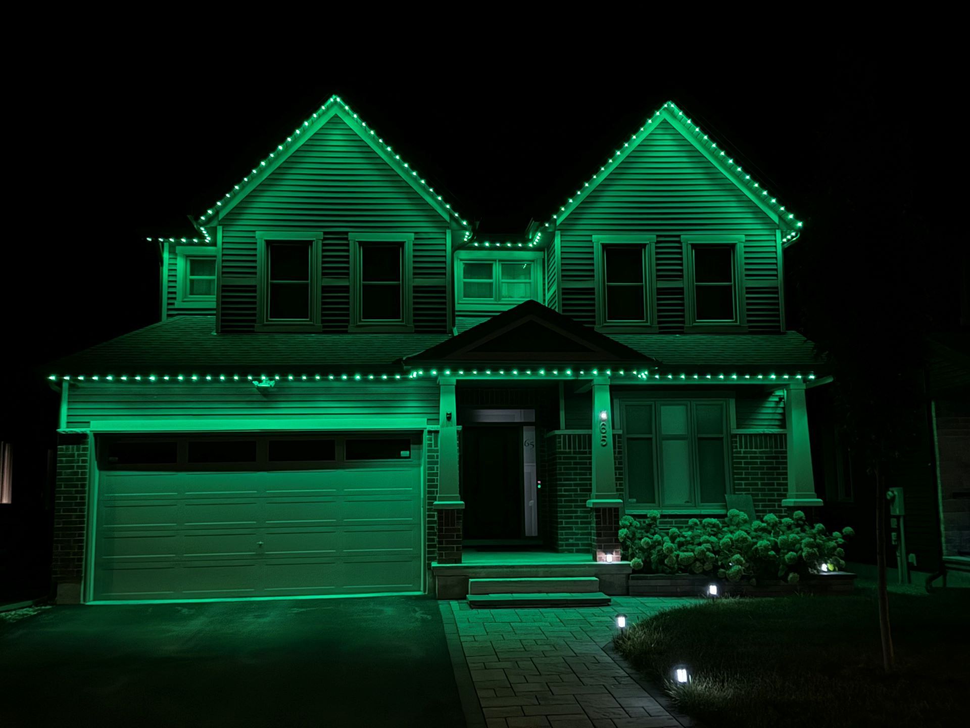 Two-story house outlined with bright green lights at night, with lit garage and front porch.