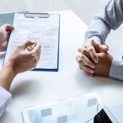 a man is sitting at a table with his hands folded in front of a clipboard at chiropractor.