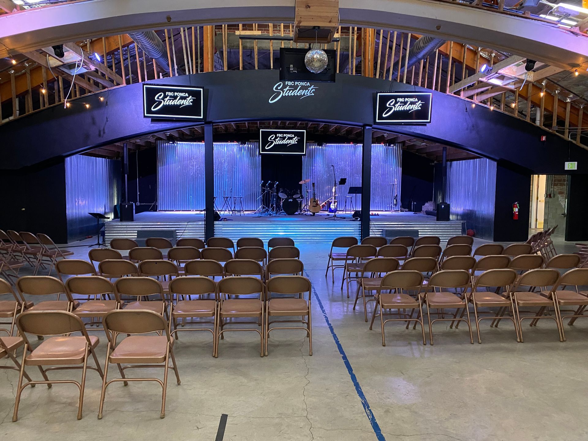 Empty venue with stage, chairs, and stage setup for a performance. Purple lighting.