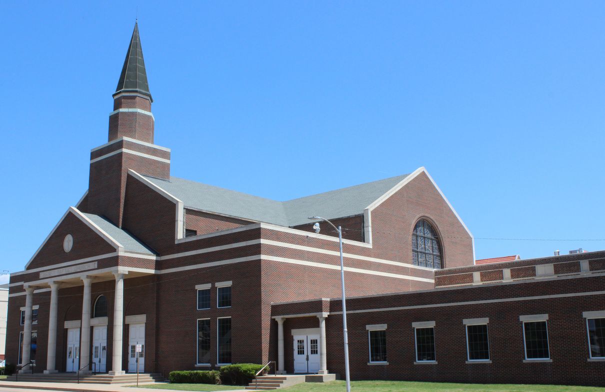 Brick church building with a steeple under a bright blue sky.