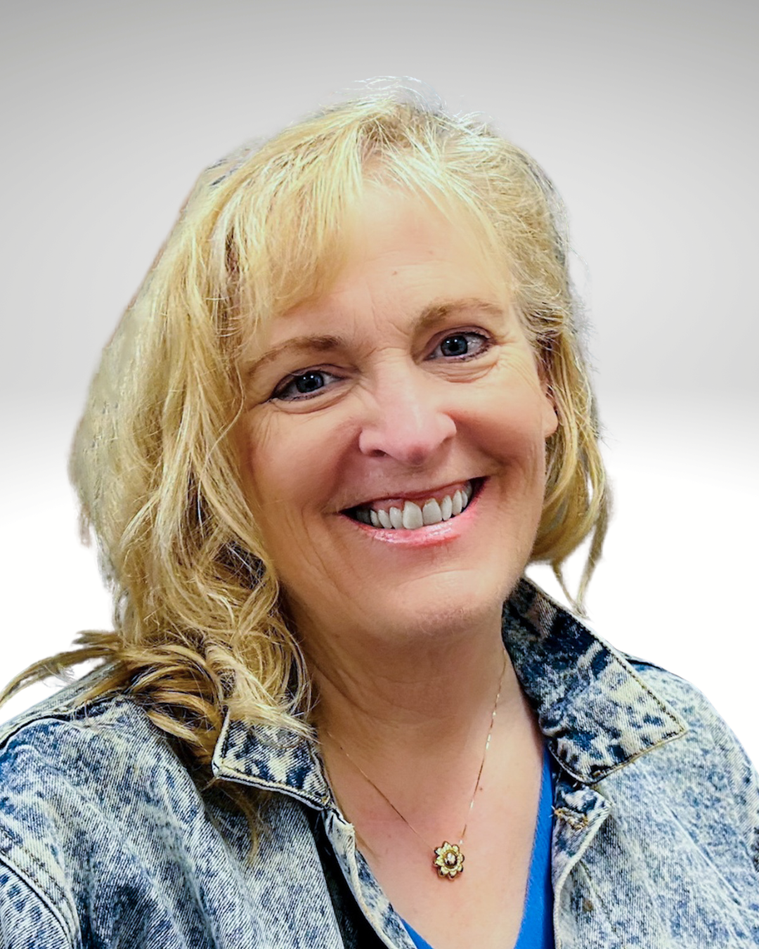 Smiling blonde woman in a denim jacket against a light background