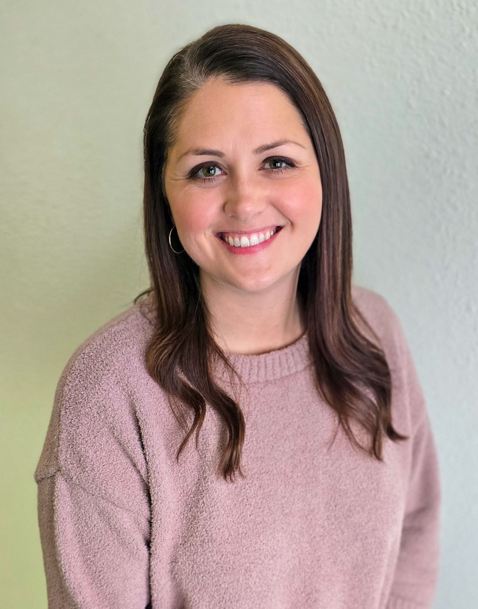 Smiling woman in a pink sweater standing against a light wall.