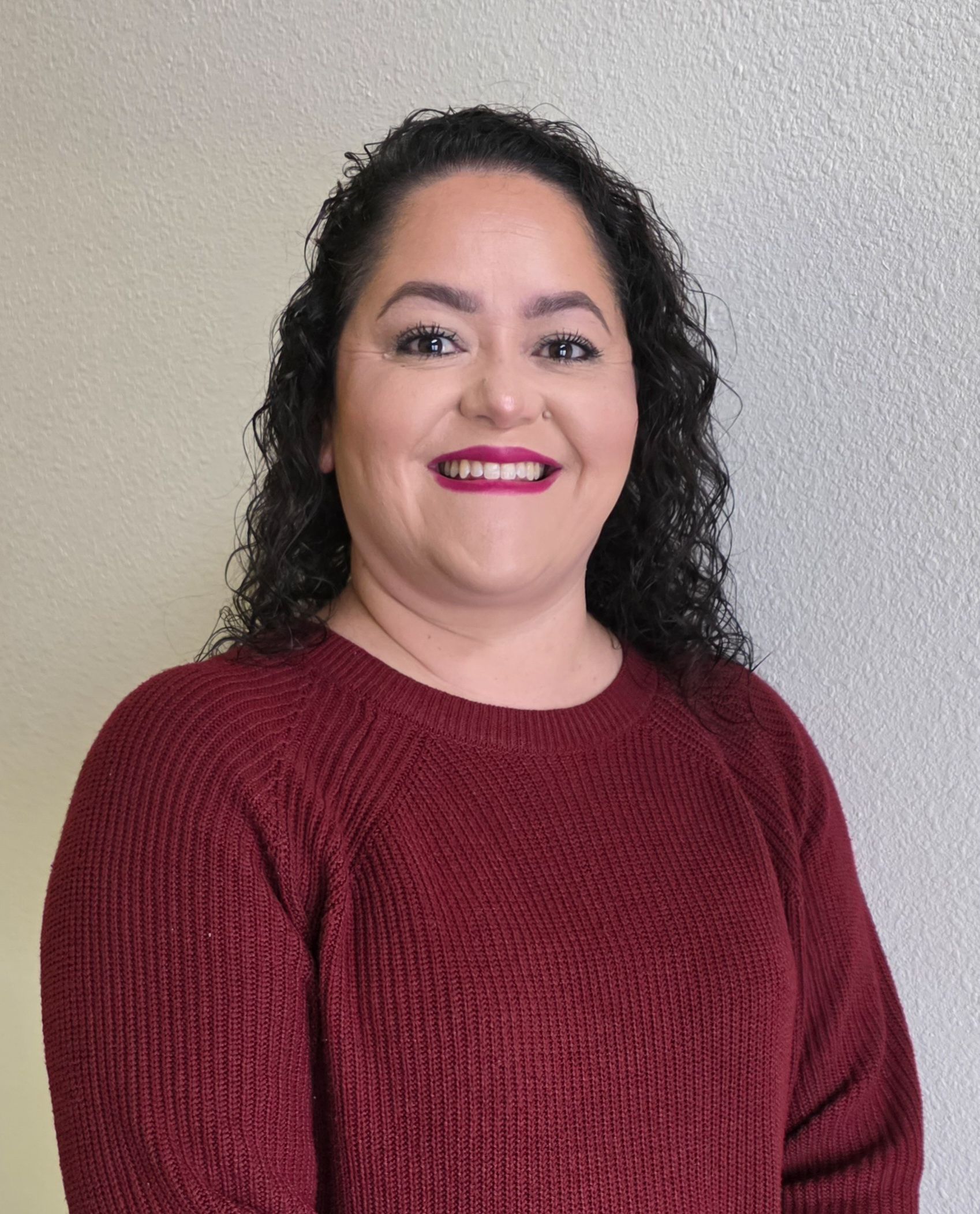 Smiling person in a burgundy sweater against a light gray wall.