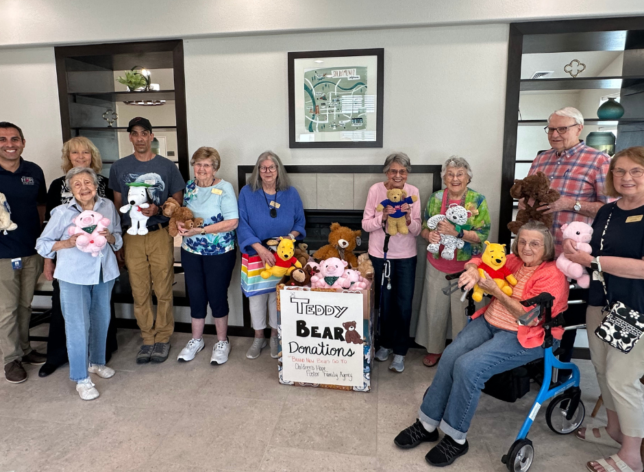A group of people are holding stuffed animals in front of a sign that says teddy bear donations.