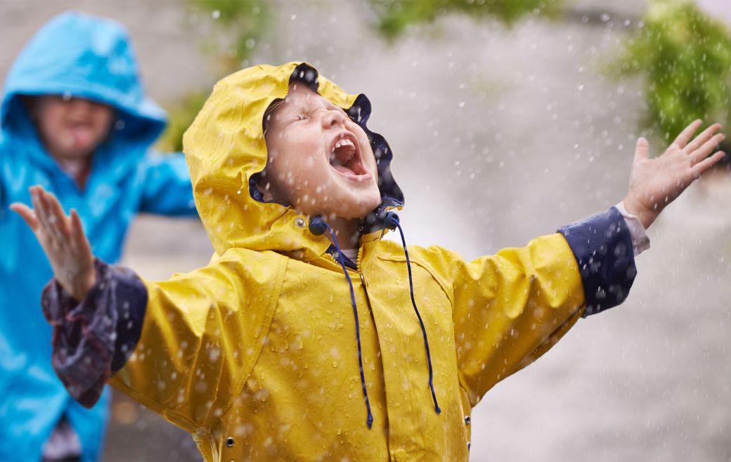 A boy in a yellow raincoat is playing in the rain.