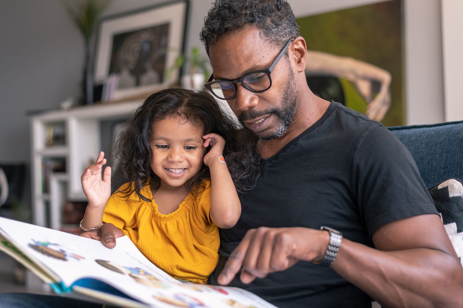 A man and a little girl are sitting on a couch reading a book together.