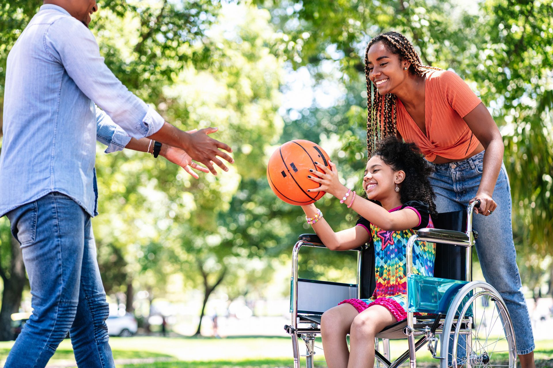 A girl in a wheelchair is playing with a basketball with her family.