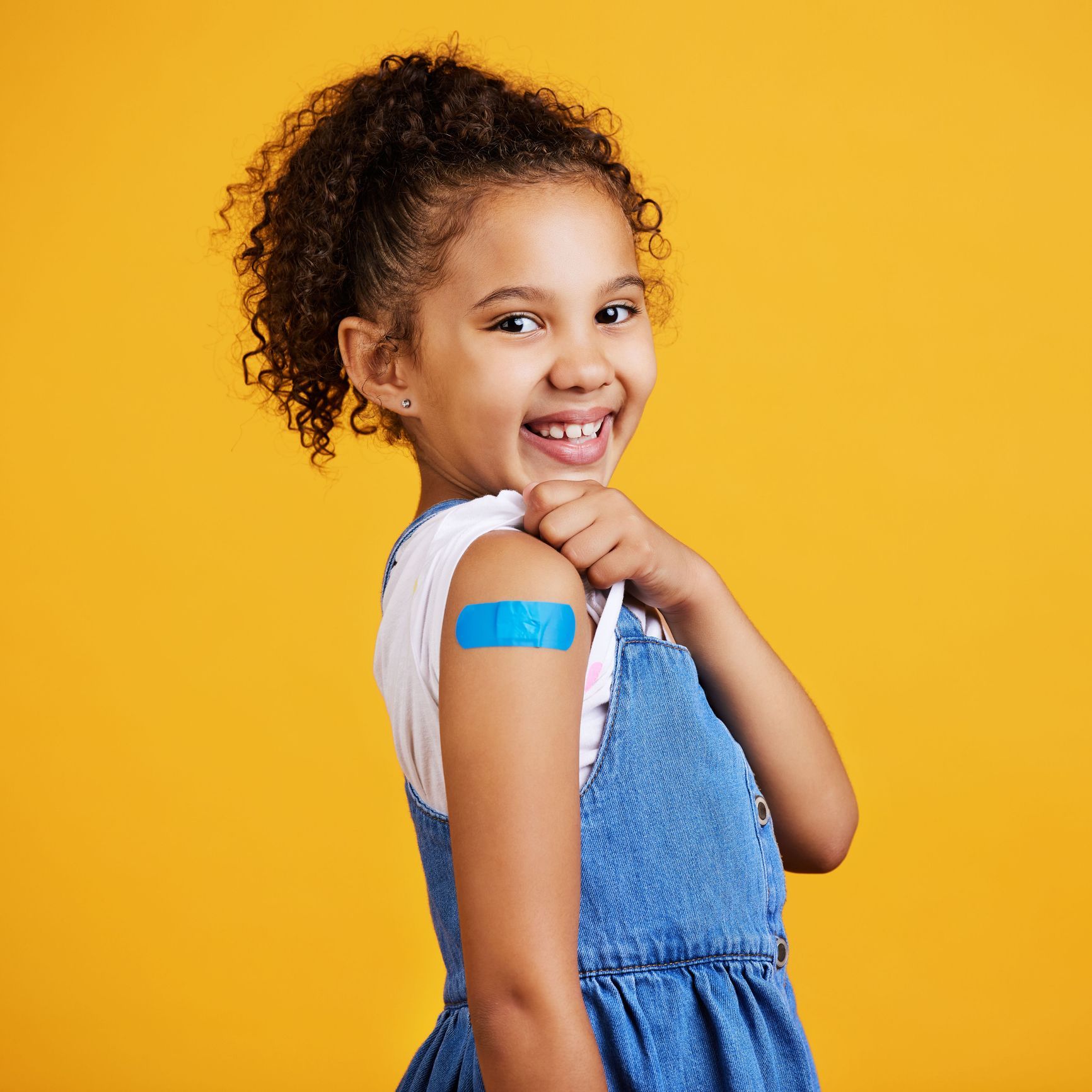 A little girl with a bandage on her arm is smiling.