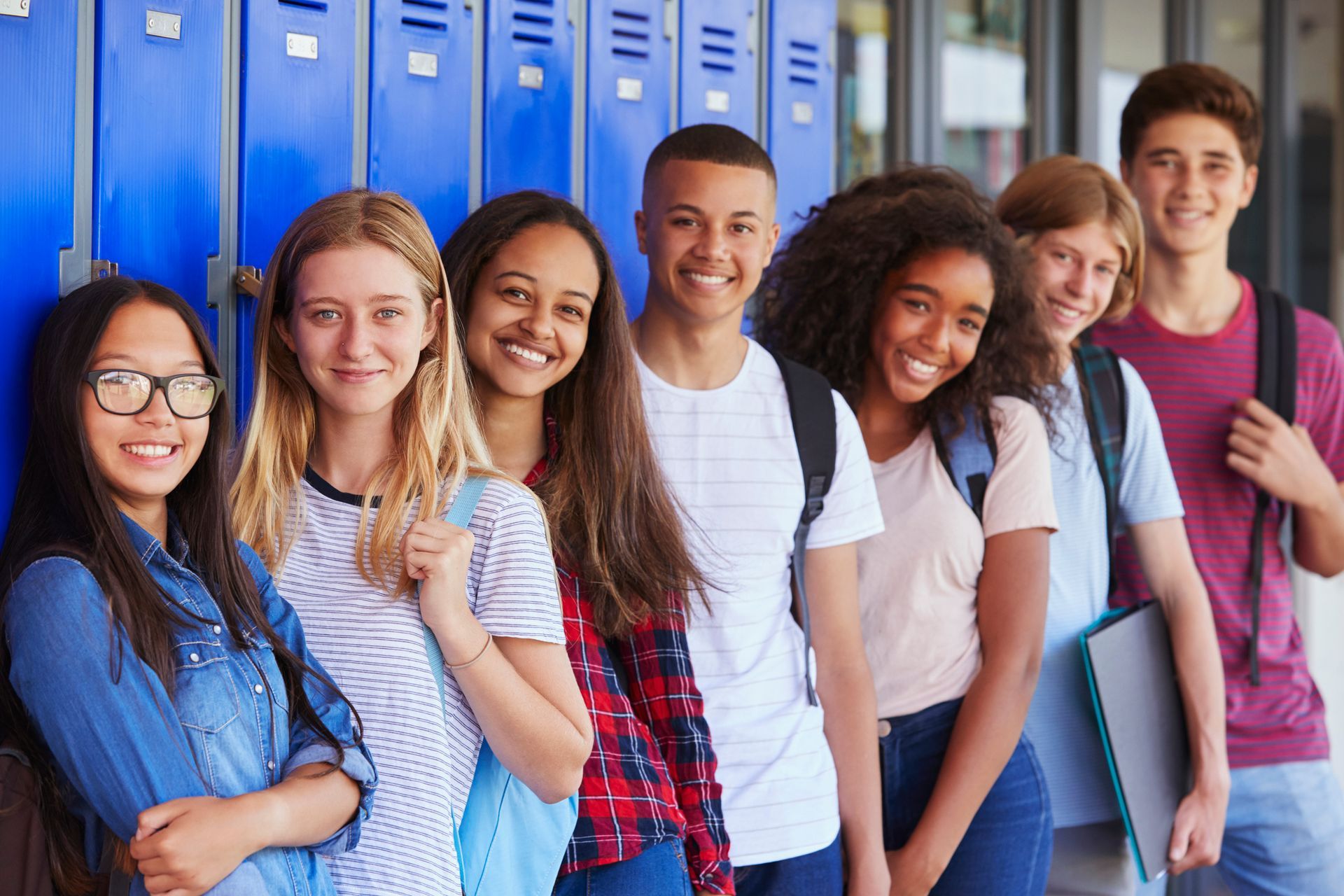 A group of young people are posing for a picture in front of blue lockers.