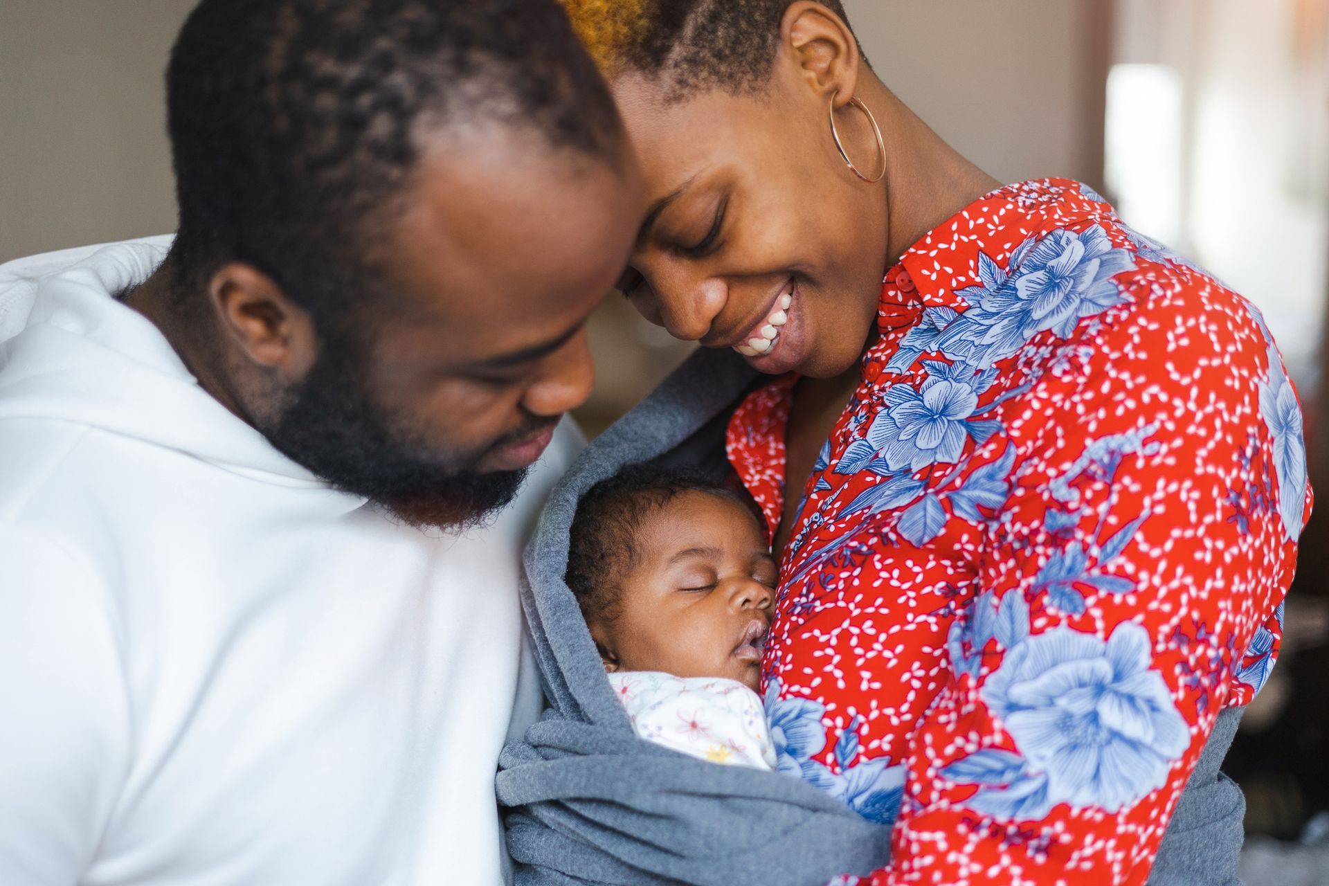 A man and woman are holding a baby wrapped in a blanket.