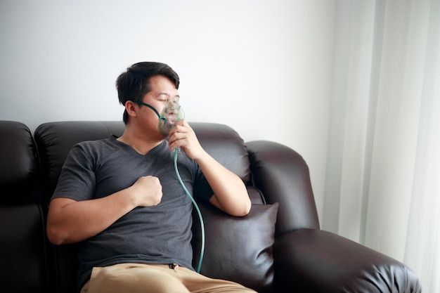 Man on couch wearing oxygen mask, indoors.