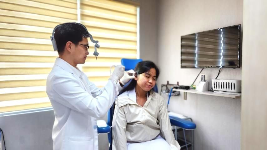 Doctor examining a seated patient in a medical examination room with a monitor and medical equipment.