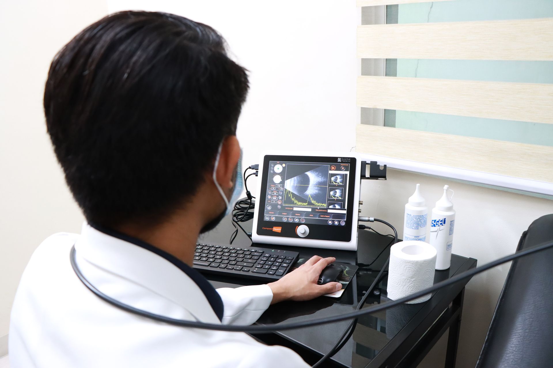 Person using a computer, potentially for medical imaging; indoors, near a window with blinds.