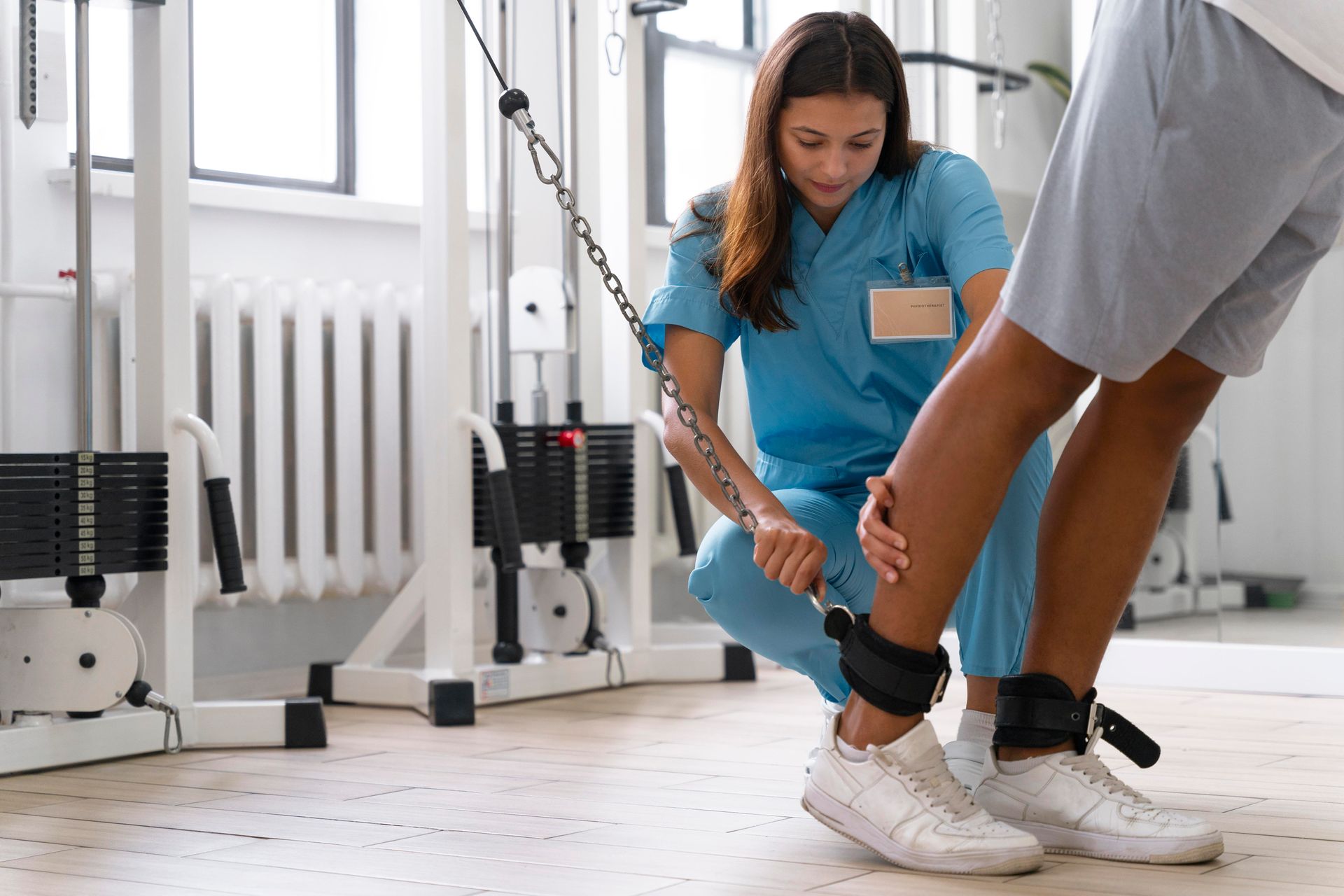 Physical therapist assisting a person with ankle exercises using a cable machine.