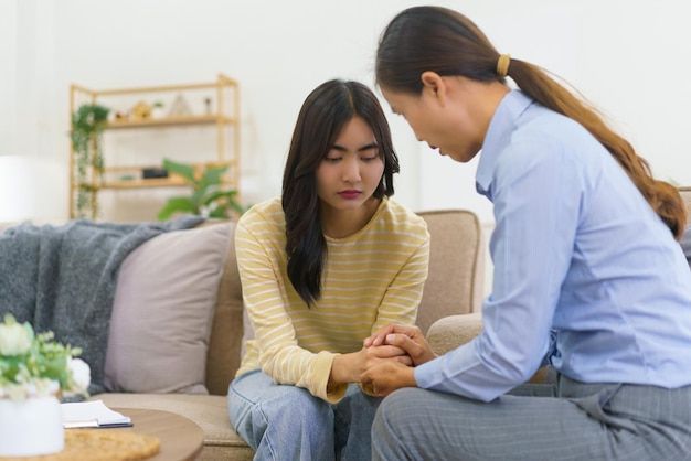 Woman comforts another, holding hands, in a living room. One looks sad, the other concerned.