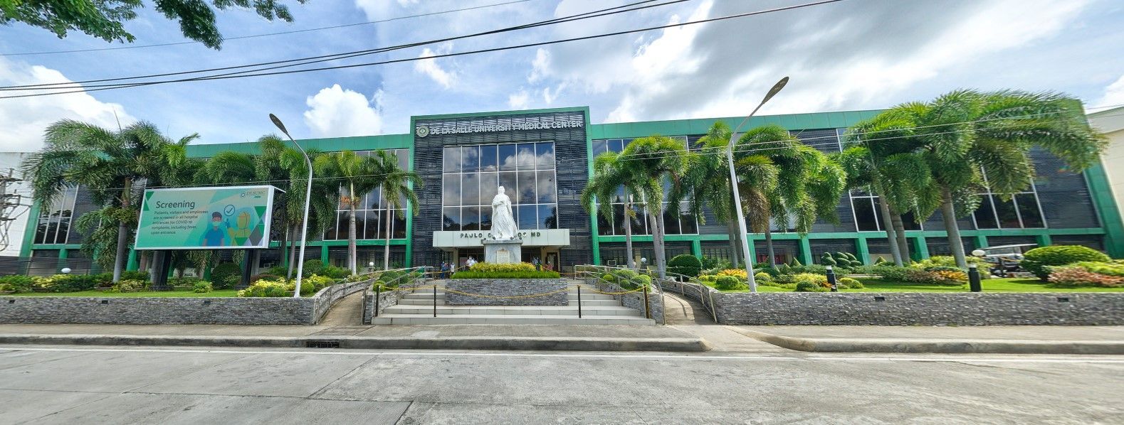 A green building with a statue in front. Trees and cloudy sky are in the background.