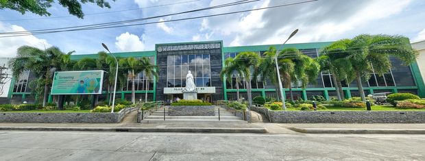 A green building with a statue in front. Trees and cloudy sky are in the background.