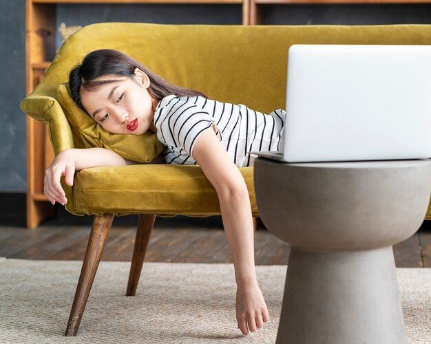 Woman asleep on a yellow sofa with a laptop on a side table.