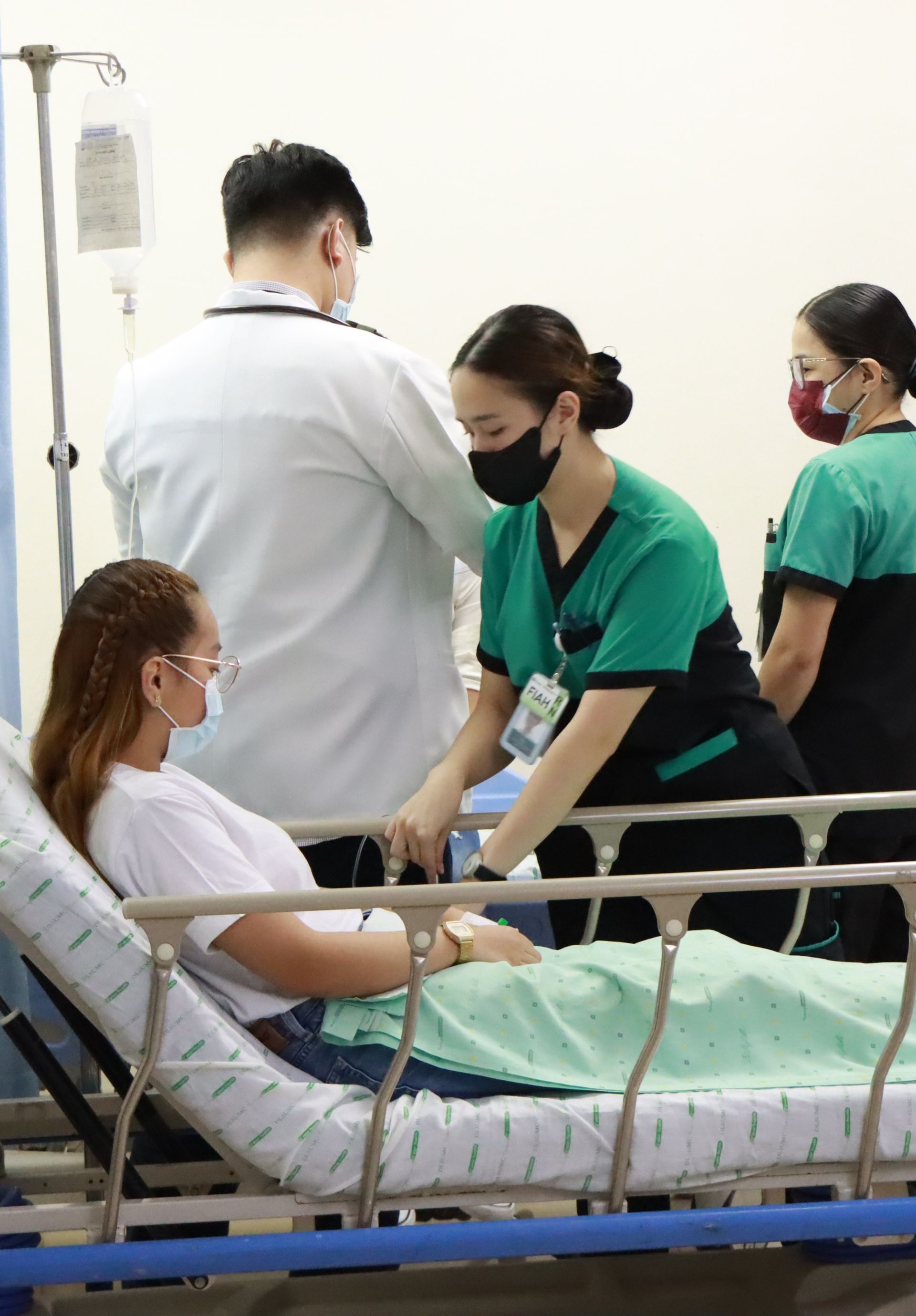Patient in hospital bed, attended by healthcare workers. Intravenous drip. All wearing masks.