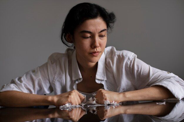 Woman in white shirt, looking down at crumpled paper on a reflective surface, hands clenched.