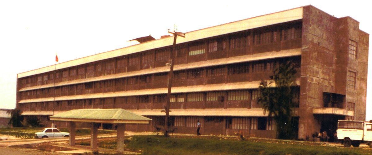 A large, three-story brick building with many windows, a covered walkway in front, and a white van parked nearby.