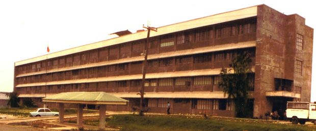 A large, three-story brick building with many windows, a covered walkway in front, and a white van parked nearby.