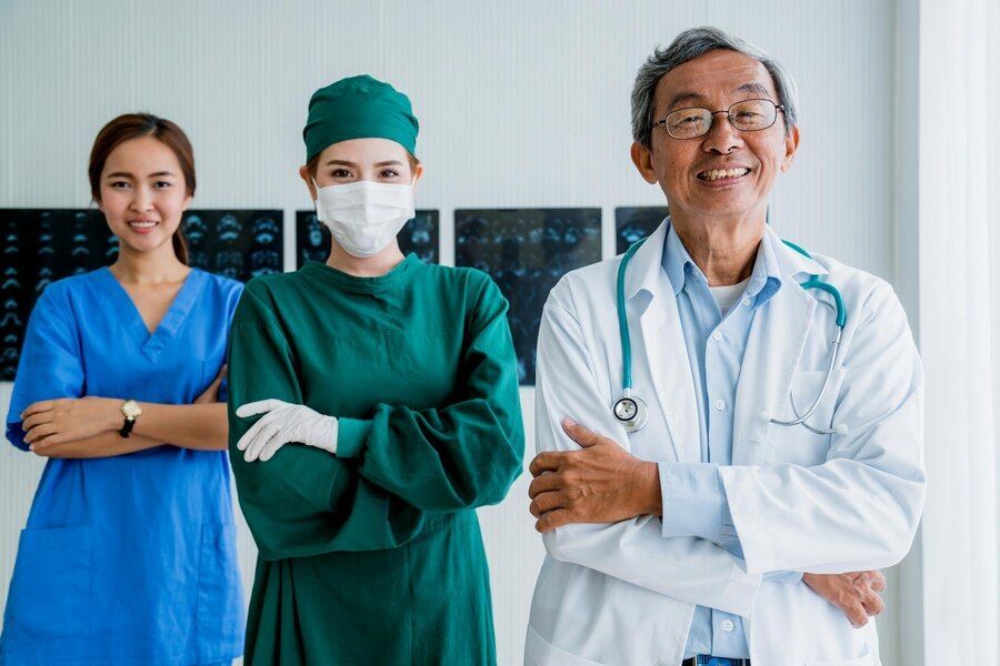 Three medical professionals in a hospital setting: a nurse, a surgeon, and a doctor, all smiling with arms crossed.