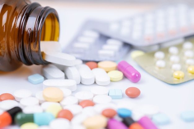 Pills of various colors spilling from a brown bottle, with blister packs in the background.
