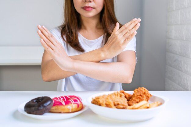 Woman crossing arms over plate of donuts and fried food, refusing unhealthy options.