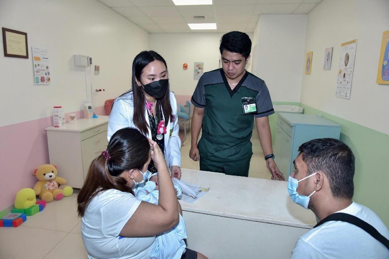 Two medical staff consult with two patients in a child-friendly hospital room.