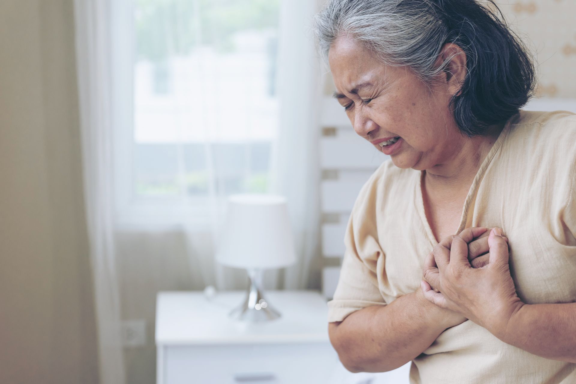 Woman clutching her chest in pain, inside a bedroom.