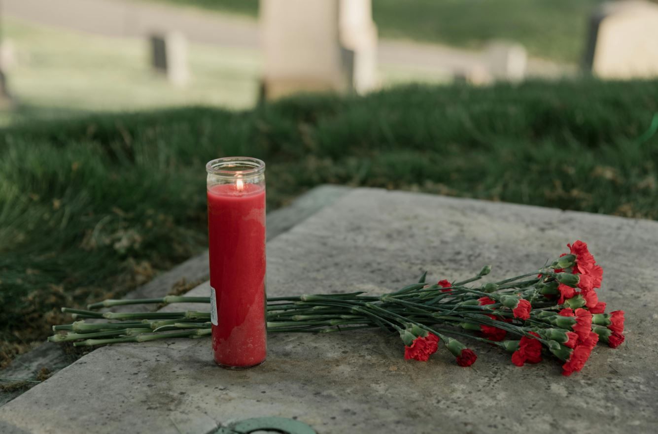 funeral remembrance scene with a prayer candle and red carnations laid at a cemetery grave in rio bravo, tx