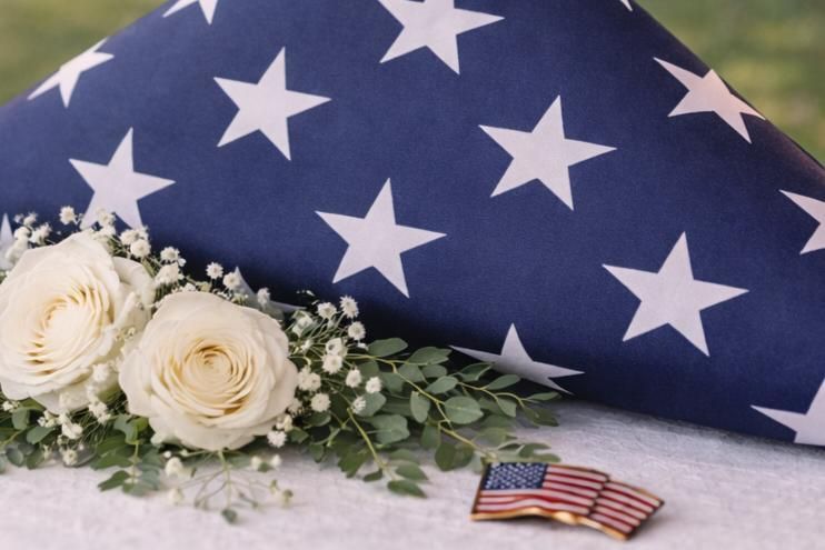 Folded American flag displayed with white roses, greenery, and a small U.S. flag pin at a military memorial service in a Funeral Home El Cenizo, TX.