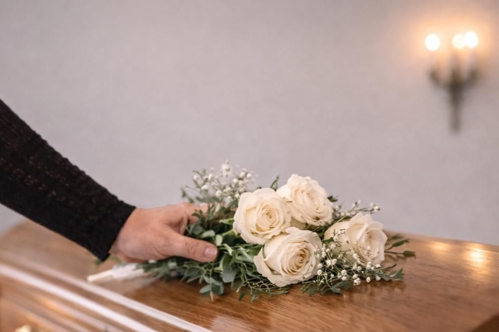 Hand placing a bouquet of white roses on a wooden casket during a memorial service, representing compassionate care and remembrance at a Funeral Home El Cenizo, TX.