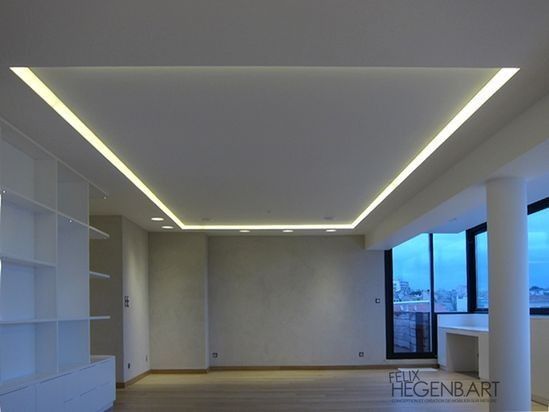Habitación moderna vacía con luces empotradas en el techo, paredes grises, estanterías y grandes ventanas.