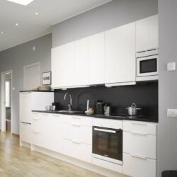 Cocina moderna blanca con salpicadero negro, electrodomésticos integrados y armarios brillantes.