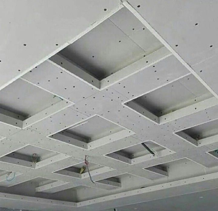 Techo de pladur blanco con una cuadrícula de aberturas rectangulares empotradas y cableado a la vista durante la construcción.