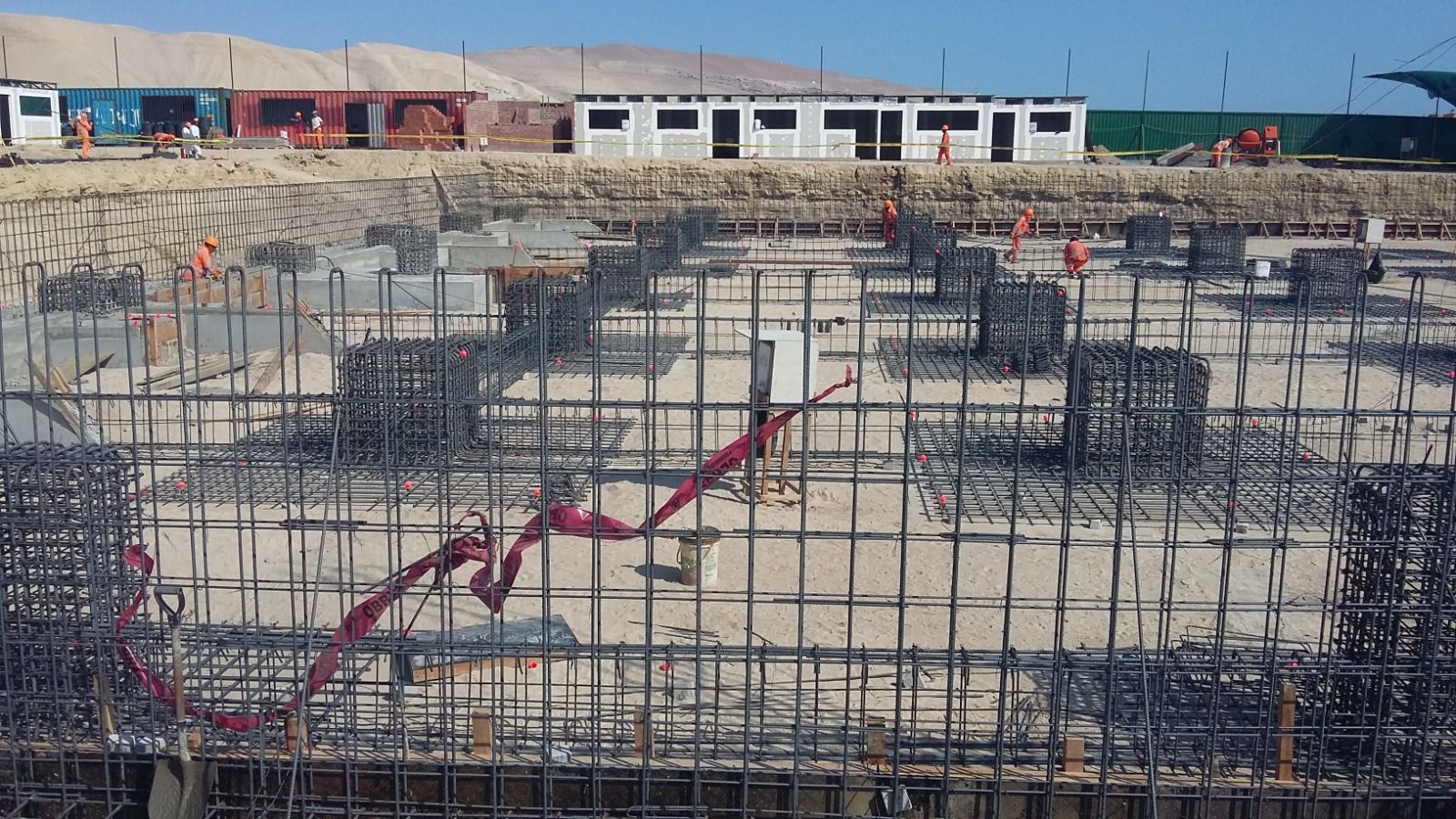 Obra en construcción con cimientos de barras de refuerzo y zapatas de hormigón en una zona amplia y abierta.