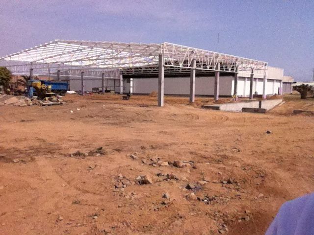Un gran edificio con estructura de acero en construcción en un terreno polvoriento y árido.