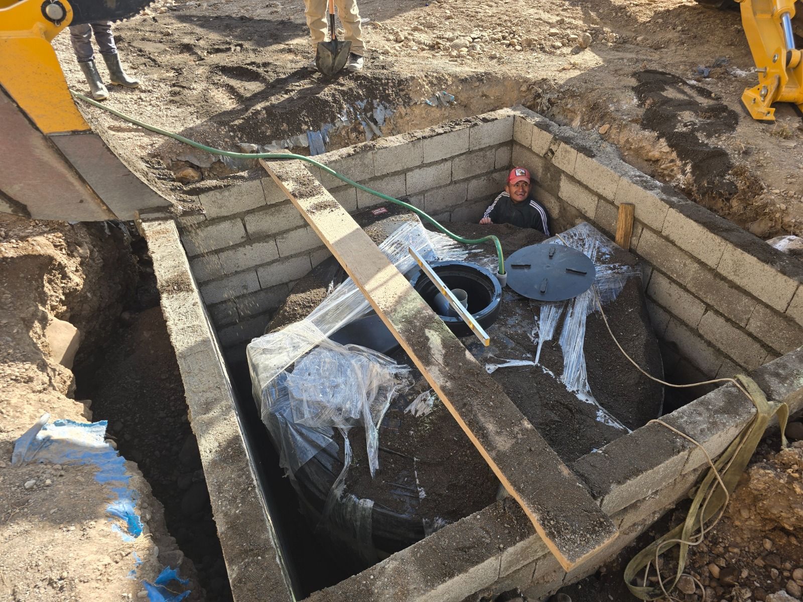 Foso de construcción con paredes de bloques de hormigón, trabajadores y una escalera sobre una excavación profunda.