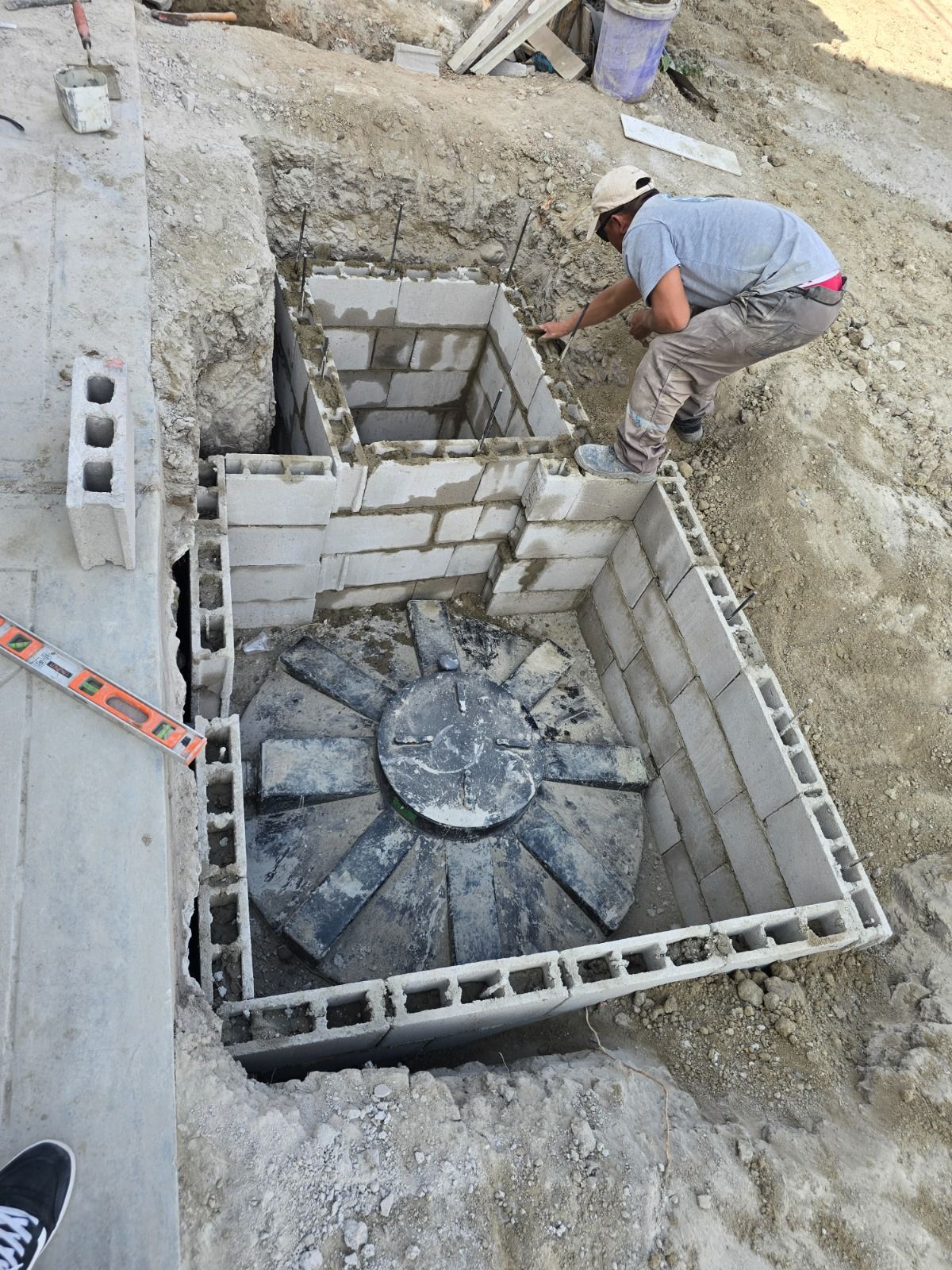Obrero construyendo una base de bloques de hormigón alrededor de una estructura circular de hormigón en una obra de construcción.