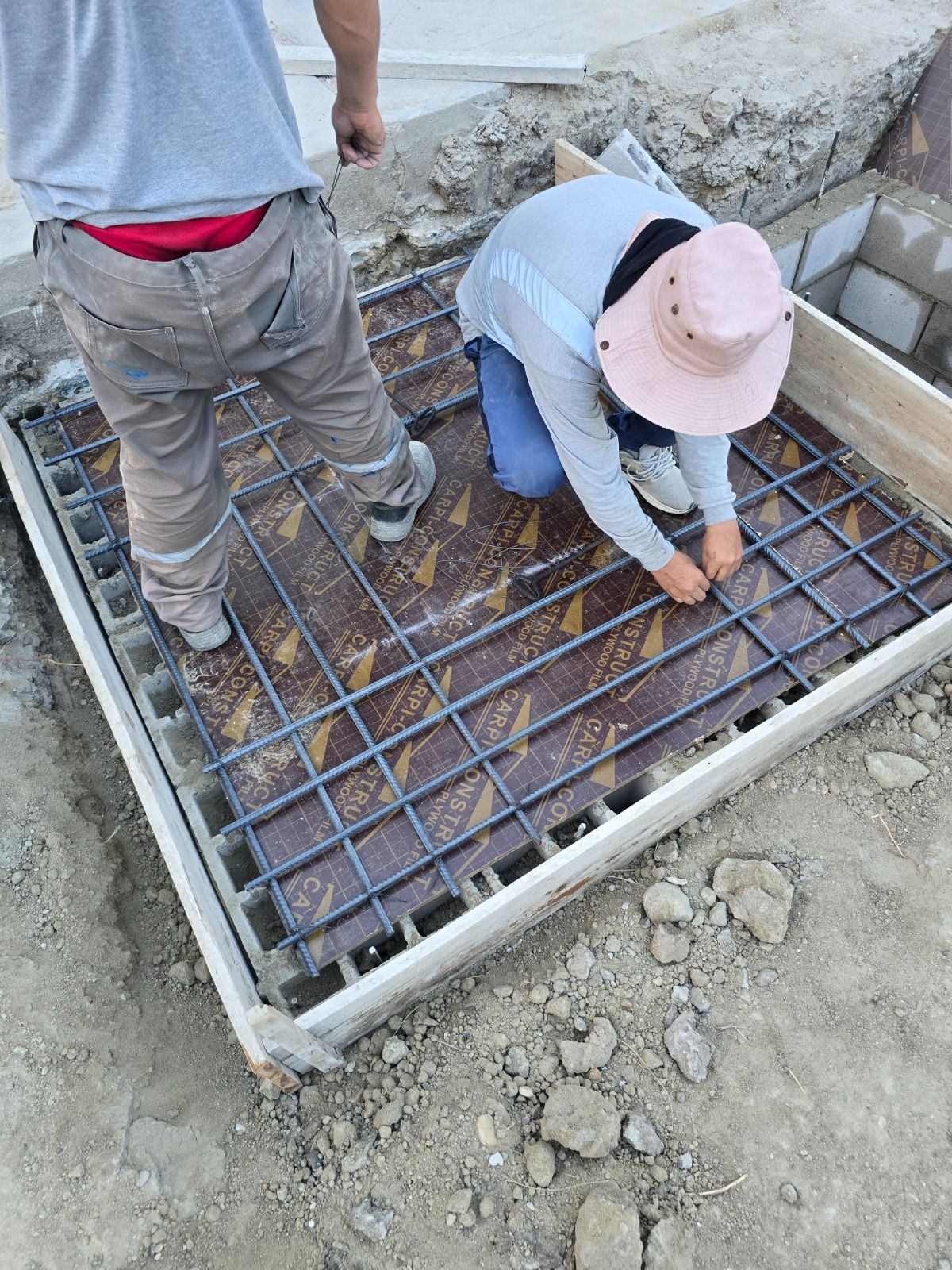 Dos trabajadores atando barras de refuerzo en un molde de hormigón en una obra de construcción.