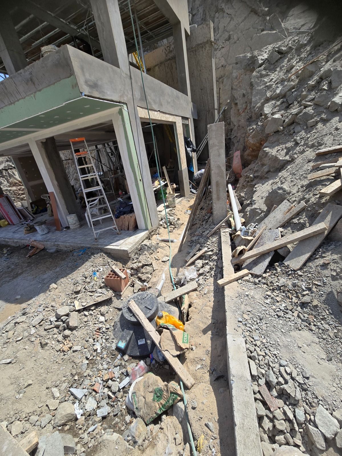 Obra dañada con escombros, hormigón expuesto y un muro derrumbado junto a una escalera y herramientas de los trabajadores.